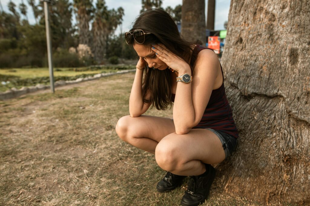 A stressed woman squatting by a tree in a park.